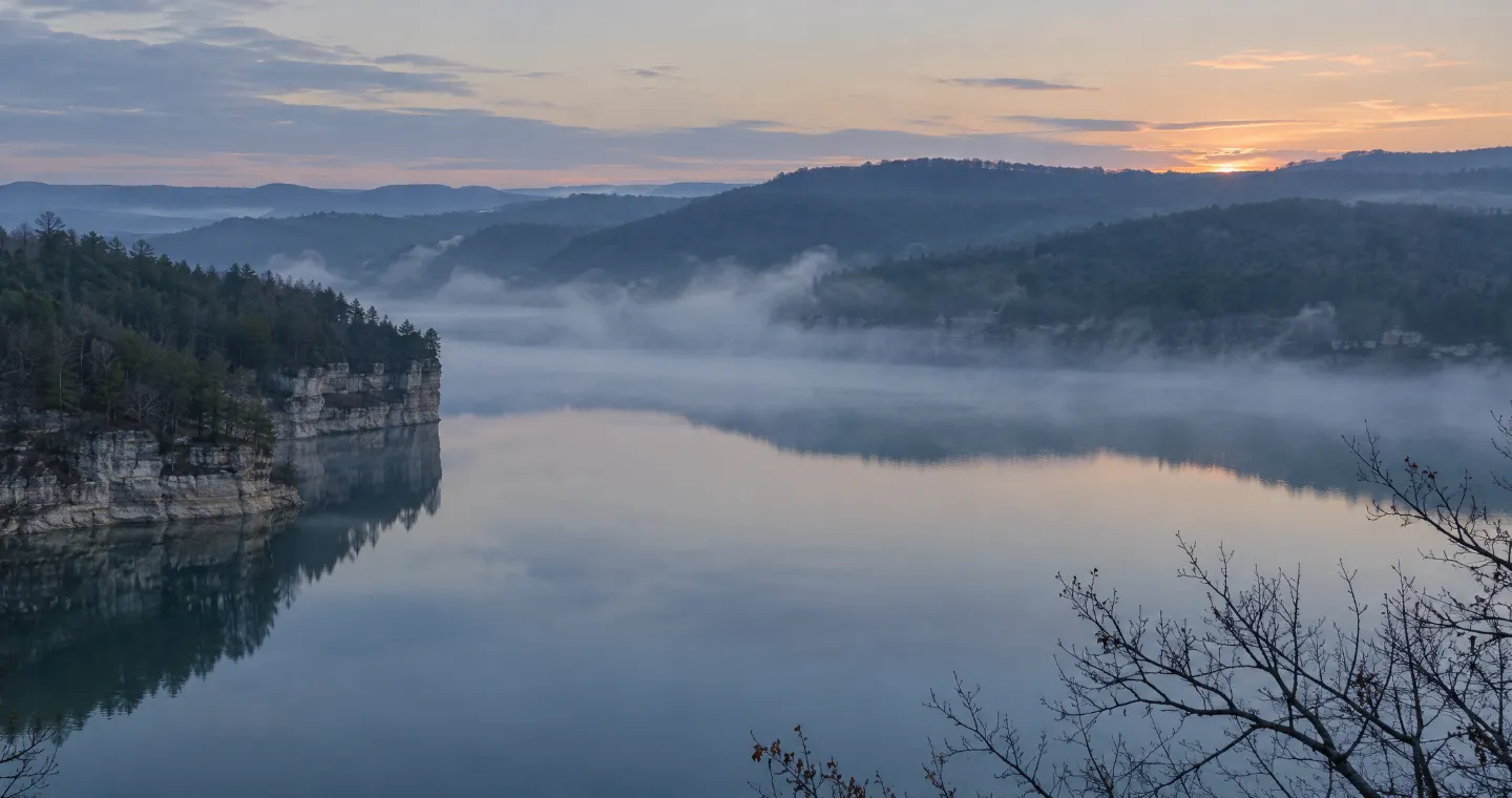 A quiet reservoir lake at dawn with mist over the water and forested ridgelines